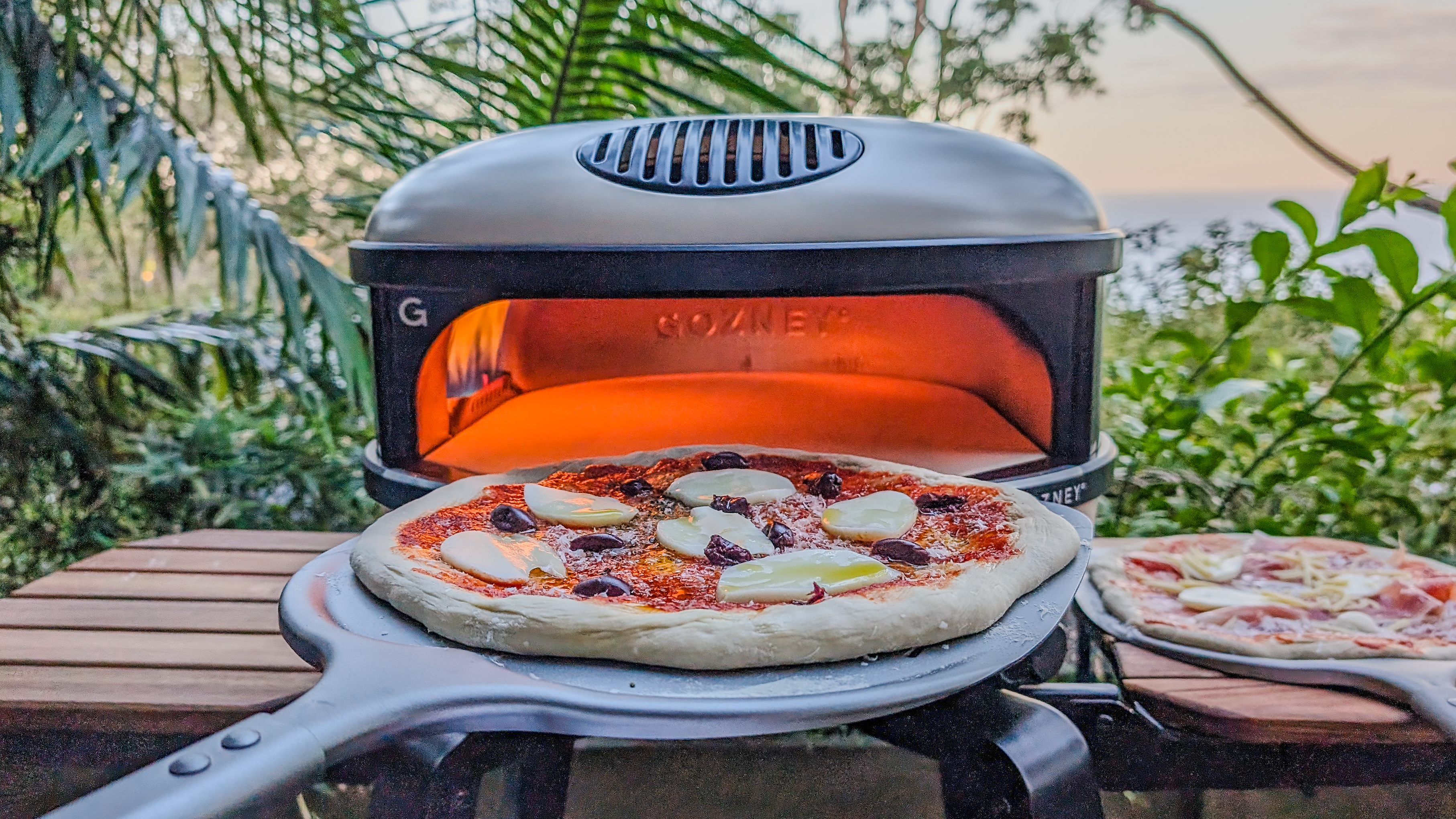 An uncooked pizza on a peel going into the fired-up Gozney Arc XL pizza oven