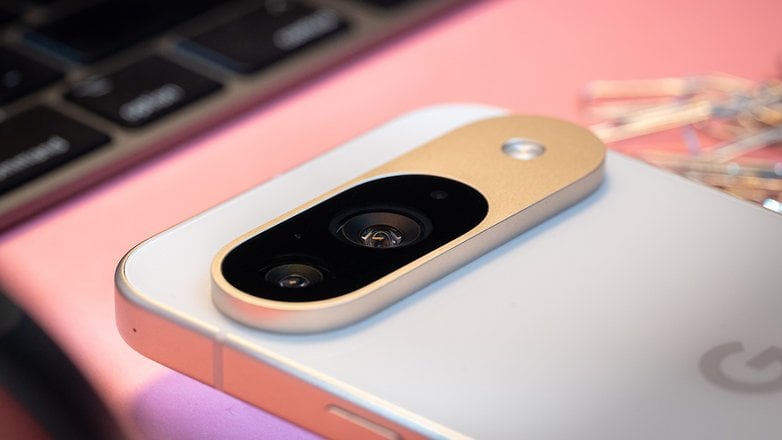 Close-up of a Google Pixel 9 smartphone's camera module on a pink surface with keys in the background.