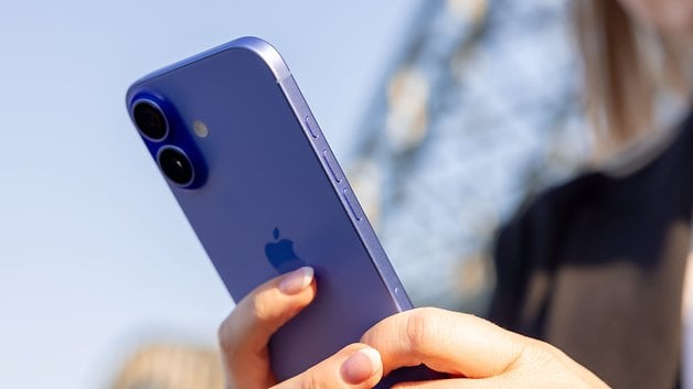 A person holding an Ultramarine iPhone 16 showing the back with dual cameras and the Apple logo.