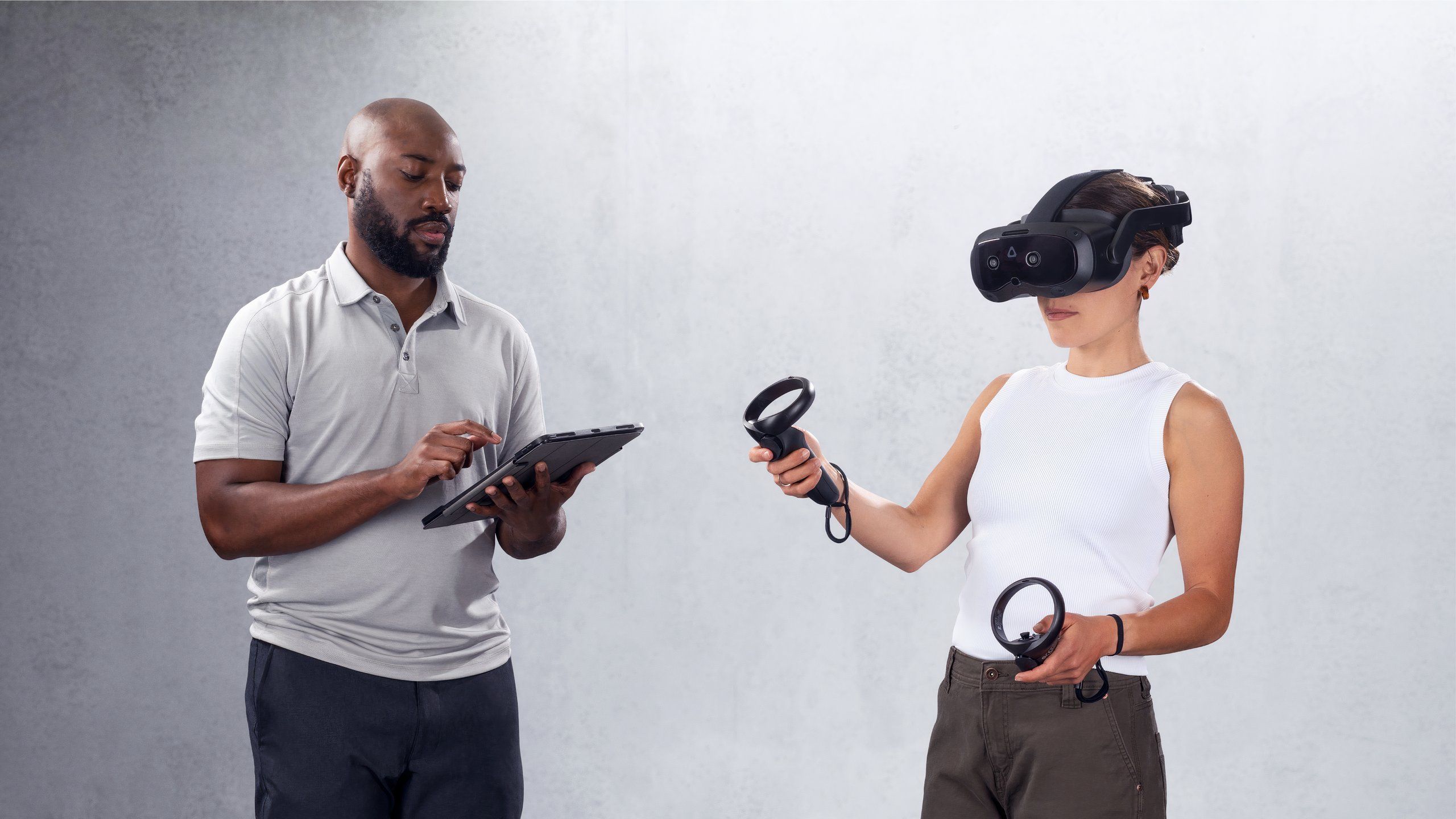 A woman wearing a Vive Focus Vision with controllers while being watched by a man with a tablet.