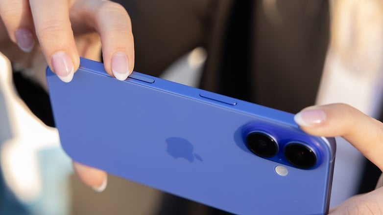 A person holding a blue iPhone-16, focusing on the buttons and dual cameras on the back.