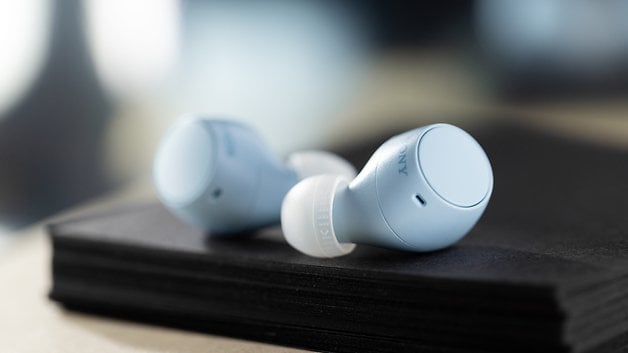 Sony WF-C510 light blue headphones resting on a stack of black paper.