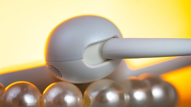 A close-up of Soundcore Aerofit 2 earbuds resting on a pearl necklace against a warm background.