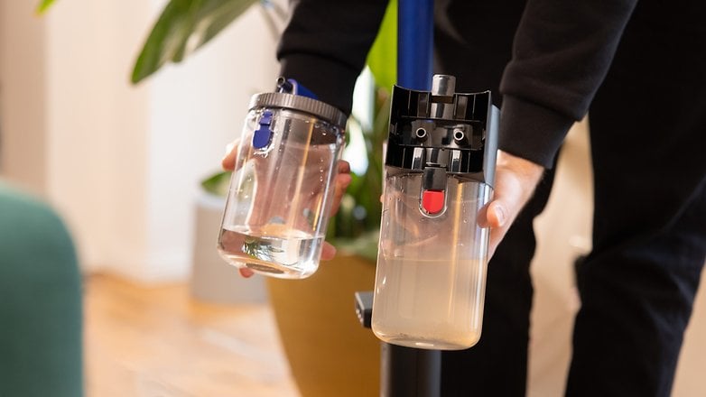 A person holding two containers: one clear with water, the other cloudy, attached to a Dyson vacuum cleaner.