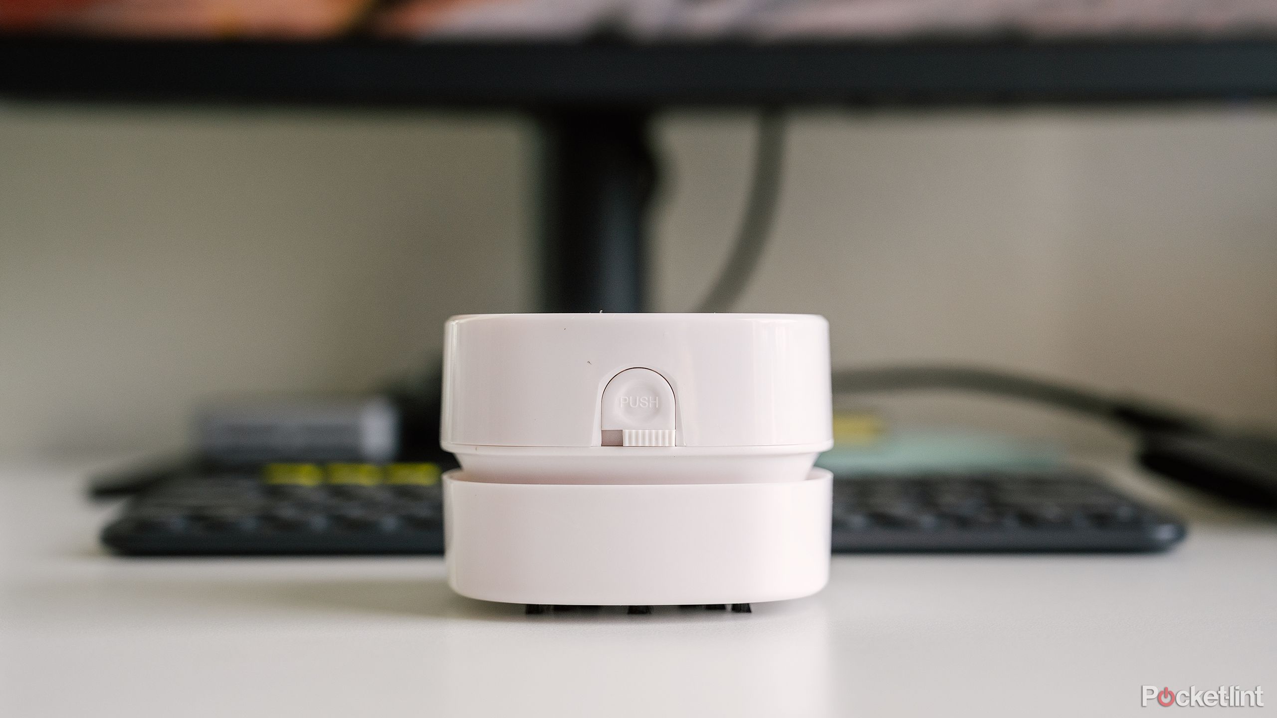 The white Odistar Desktop Vacuum Cleaner sits on a desk in front of a keyboard and a monitor.