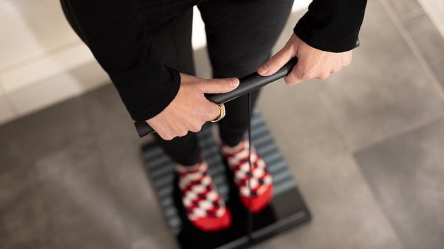 Person standing on a Withings Body Scan scale, holding the device's handle.