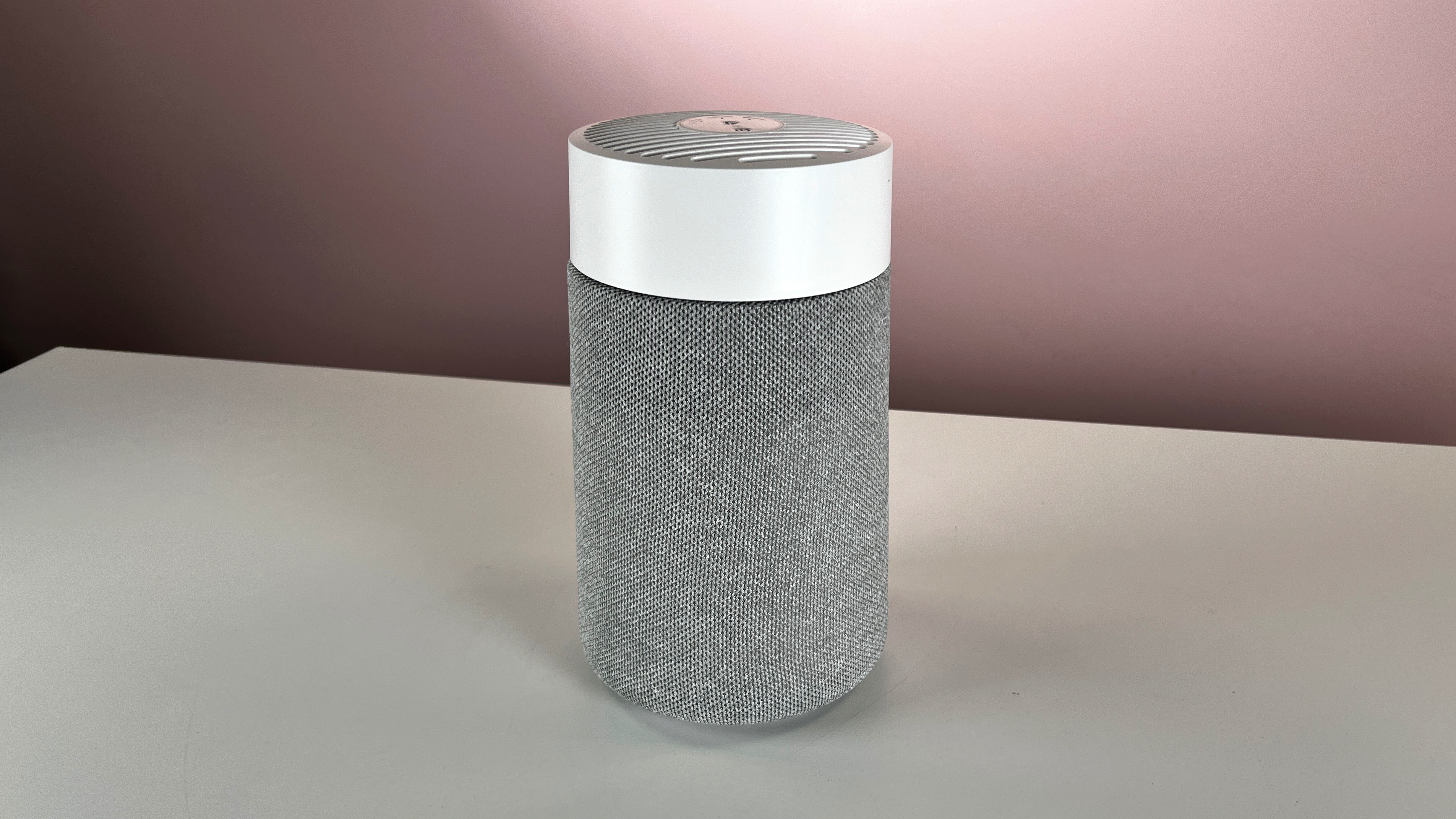 The white and gray Blueair Blue Pure Mini Max sits on a pale surface in front of a pink background.