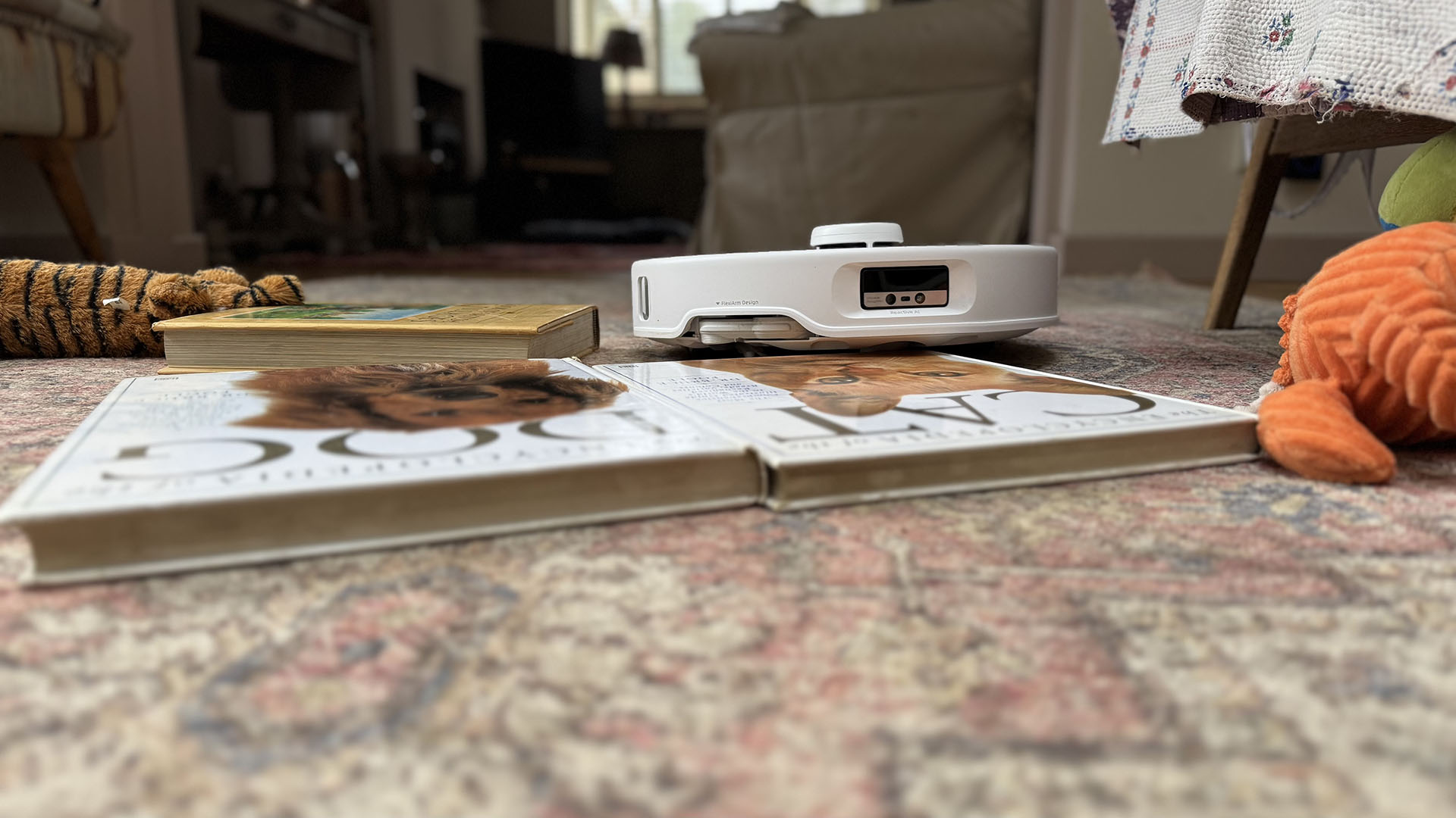 Roborock Qrevo Curv robot vacuum surrounded by tall books, to show how it can get over tall thresholds