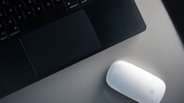 Overview of an Apple MacBook Pro M4 with touchpad and a white Apple mouse on a table.