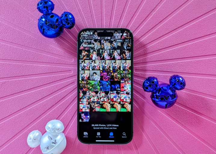 iPhone 14 Pro showing Photos app camera roll with Mickey jingle bells on pink background