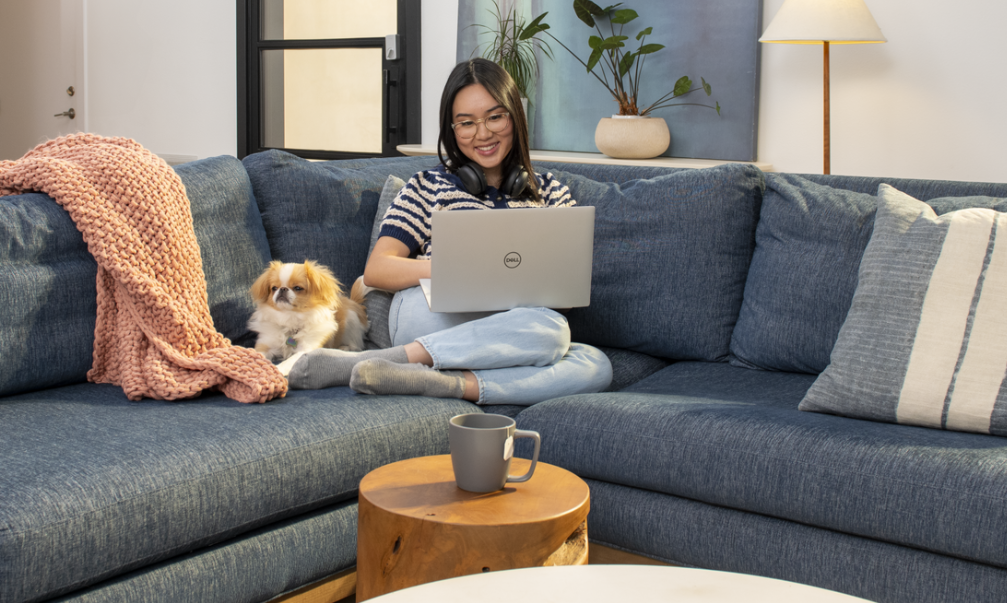 Lady sitting on a couch with a dog and a Dell laptop